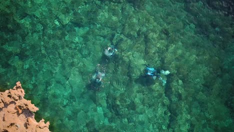 Drone-shot-above-divers-creating-water-bubbles-in-crystal-clear-seas-in-Cirkewwa-Malta