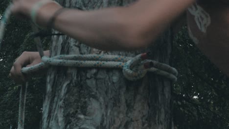 forearms and hands of a male person tying a rope around a tree trunk