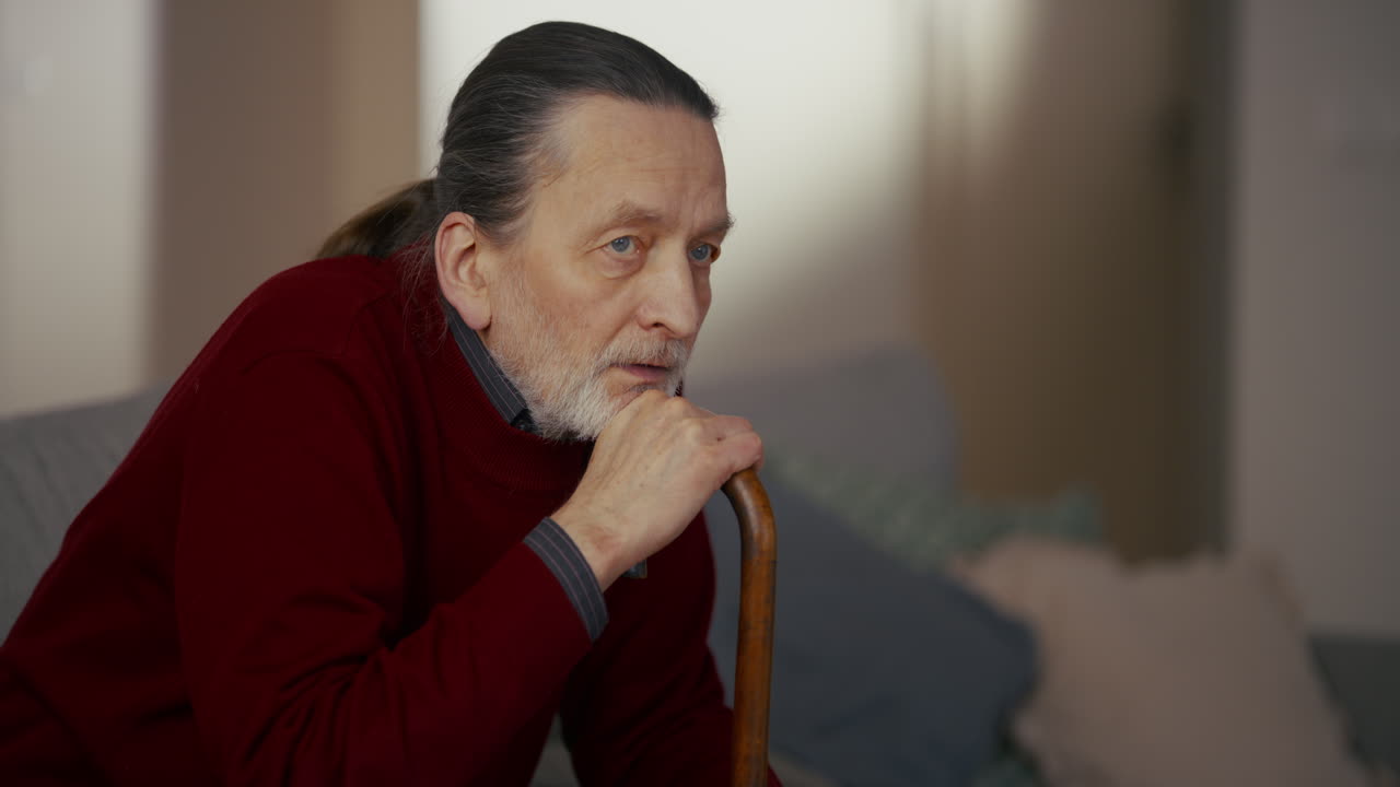 Pensive Elderly Man Sitting Indoors with a Walking Stick