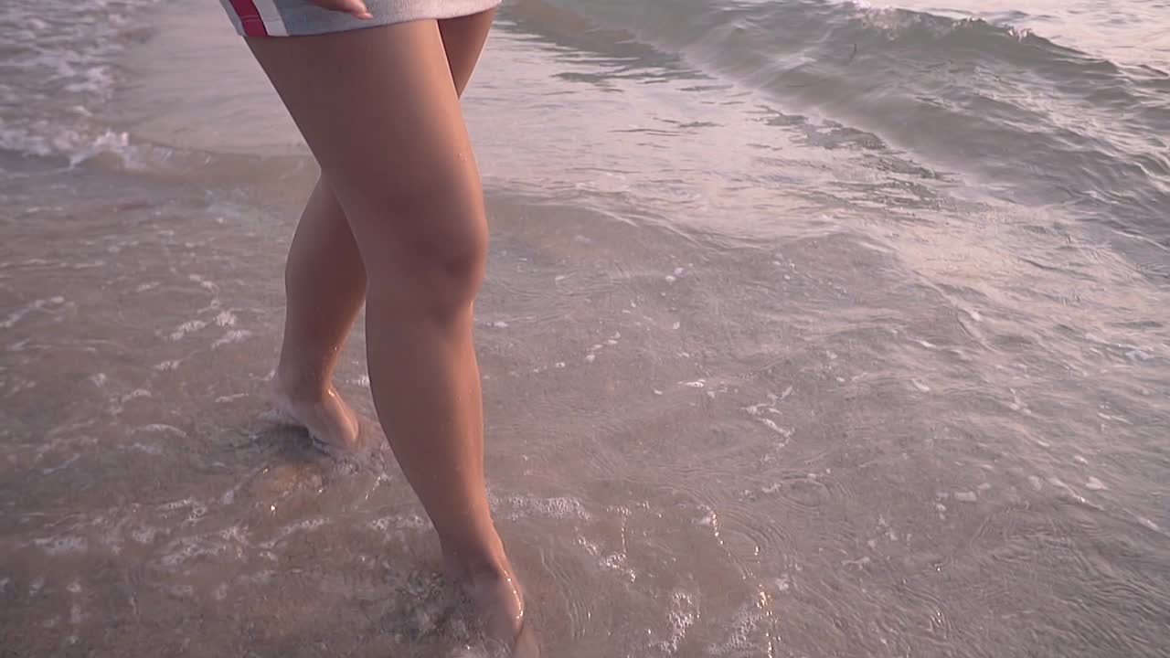 una signora felice con i capelli lunghi cammina lungo la spiaggia al rallentatore