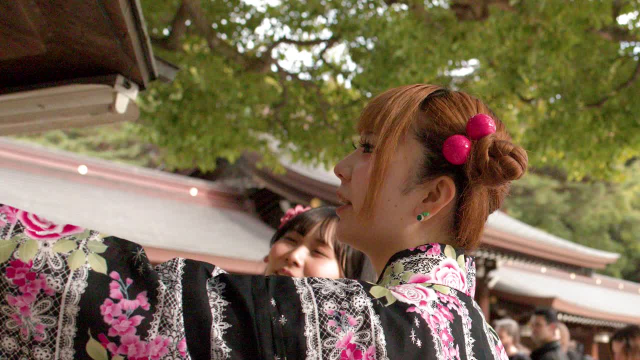 En kvinna iklädd en traditionell kimono granskar bönplaketter i trä vid en japansk shintohelgedom.