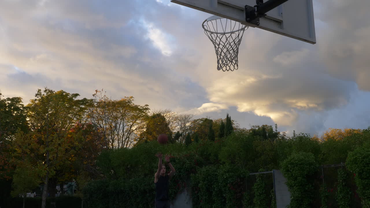 hombre practicando un tiro de dos puntos jugando solo en la cancha de baloncesto durante la puesta de sol en vancouver, canadá - tiro medio