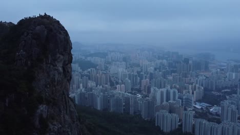 gorgeous aerial drone footage of the city hong kong in china during a misty foggy or smog covered dusk or dawn day with a large mountain ricky cliff in the foreground. tall building visible in city.