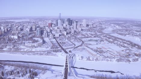 aerial rise over modern developing winter snow covered city in downtown edmonton alberta right past the snow coved north saskatchewan rivers with 3 bridges connecting