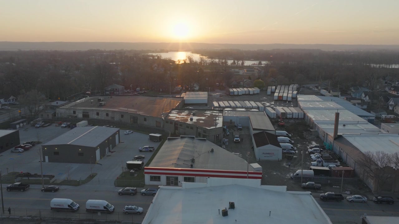 Prospettiva aerea sul distretto industriale di Omaha, Nebraska, al tramonto, con magazzini, semirimorchi, parcheggi e il fiume Missouri che risplende all'orizzonte.
