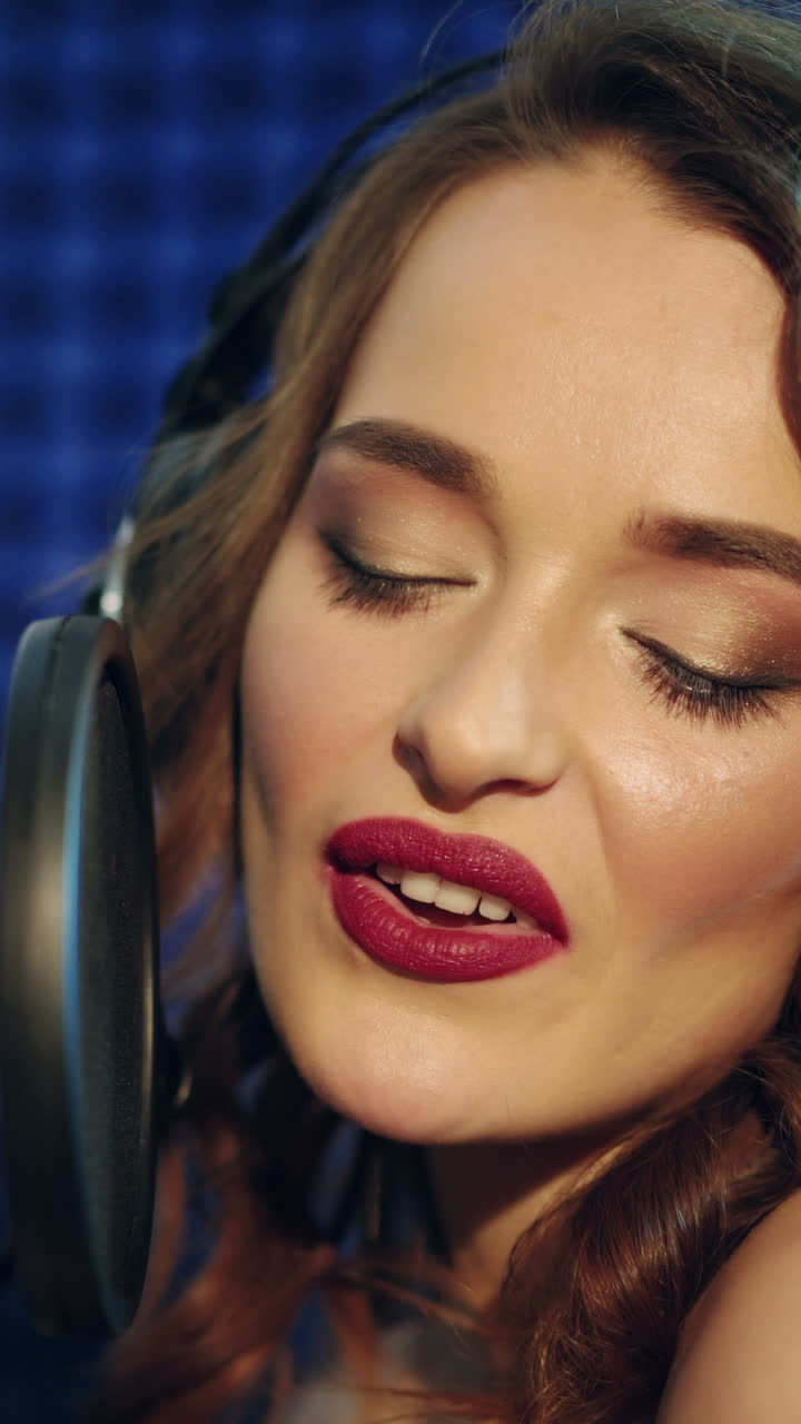 Vinnitsa, Ukraine - May 2019: Young woman recording a song in a professional studio. The girl sings into the microphone. Vertical video