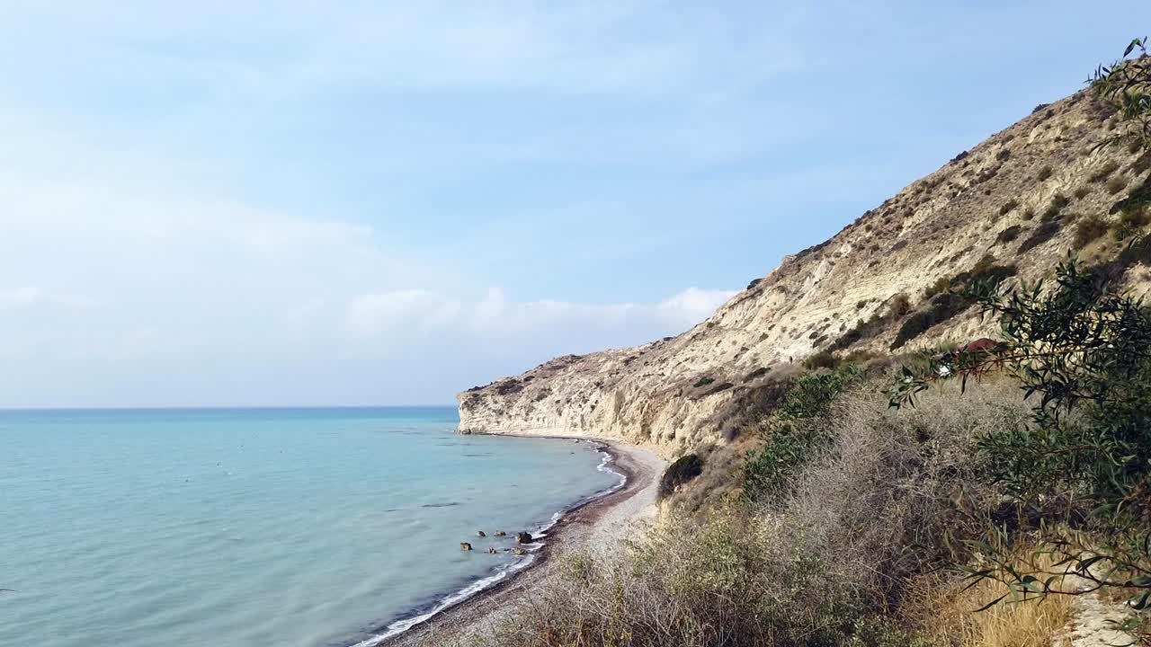 From a Pissouri car park, along a coastal path toward the beach. The Mediterranean sparkles below, with waves crashing along the beach under the warm Cyprus sun.