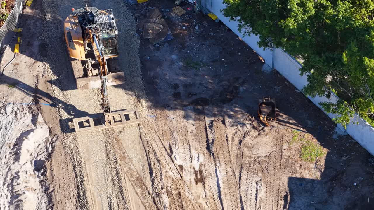 Excavator loads dirt into truck at sunny construction site, captured by moving aerial drone camera