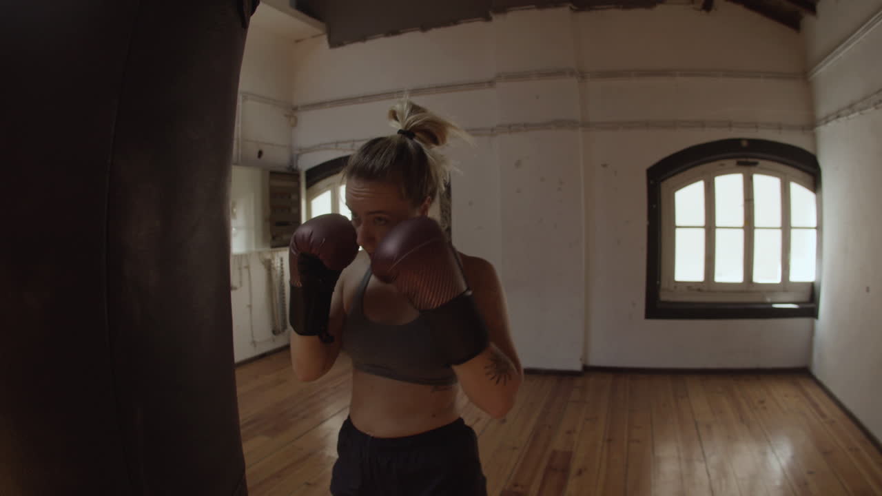 Plano de acompanhamento de mulher com luvas de boxe socando saco de pancadas