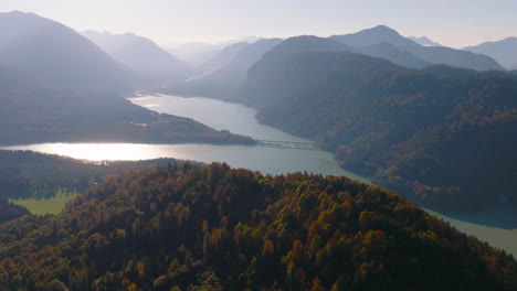 faller-klamm-brücke crossing sylvenstein lake surrounded by bavarian woodland forest and hazy mountain range aerial view