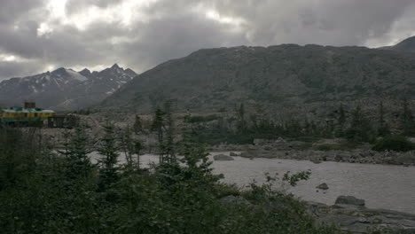 Rocky-Alaskan-Mountains-Stehen-Hinter-Einem-Kleinen-Fluss,-Der-Von-Einem-Schnell-Fahrenden-Zug-Geschossen-Wird