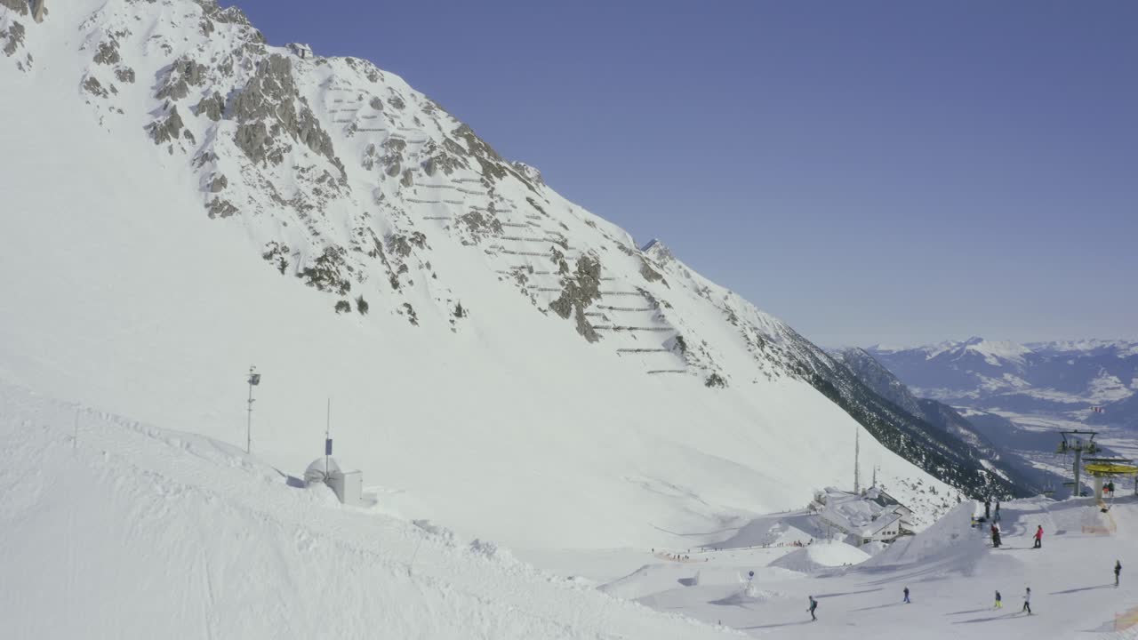 sobrevuelo de la estación de esquí de nordkette sobre innsbruck, parque de terreno del horizonte revelado sobre una cresta nevada con telesilla, alpes austríacos drone pan down