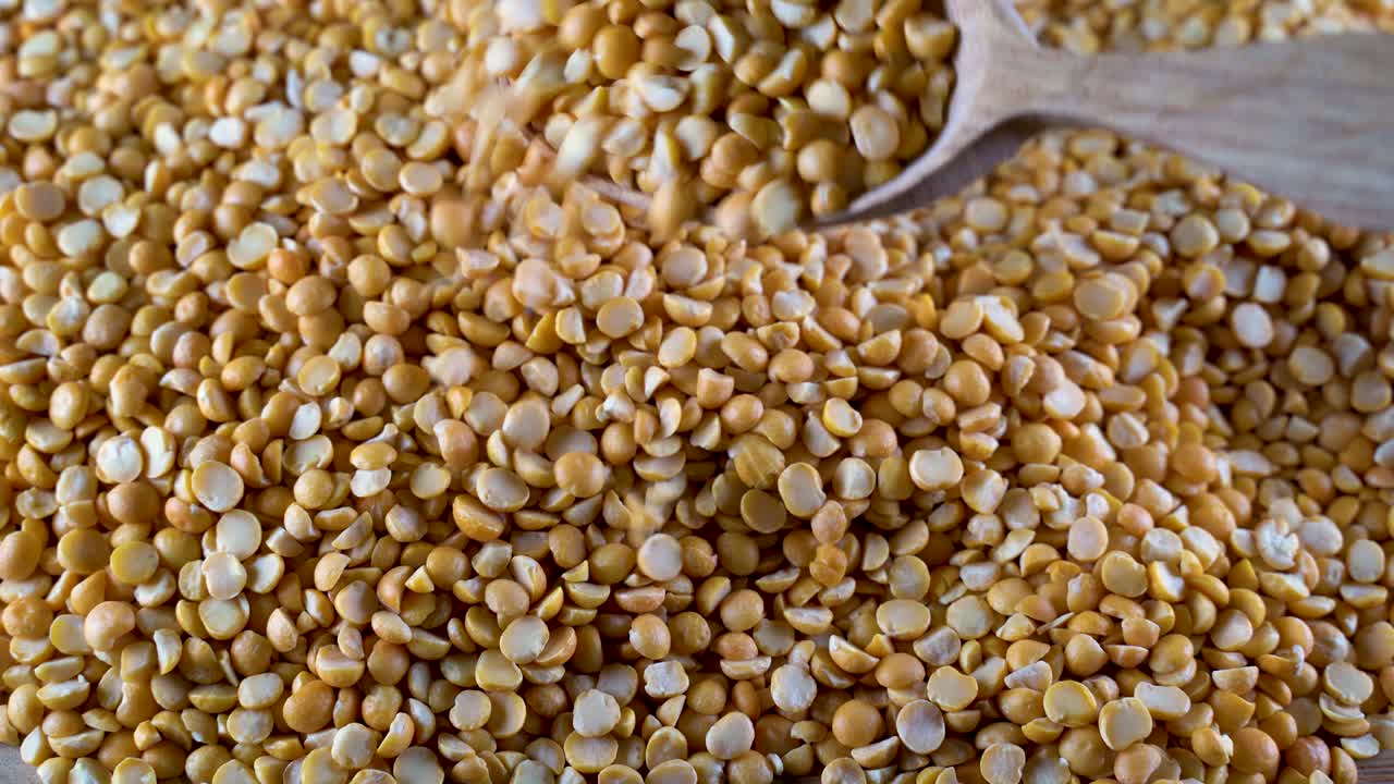 una pila de guisantes amarillos con una cuchara de madera en la mesa. legumbres altas en proteínas, frijoles y lentejas para una dieta saludable