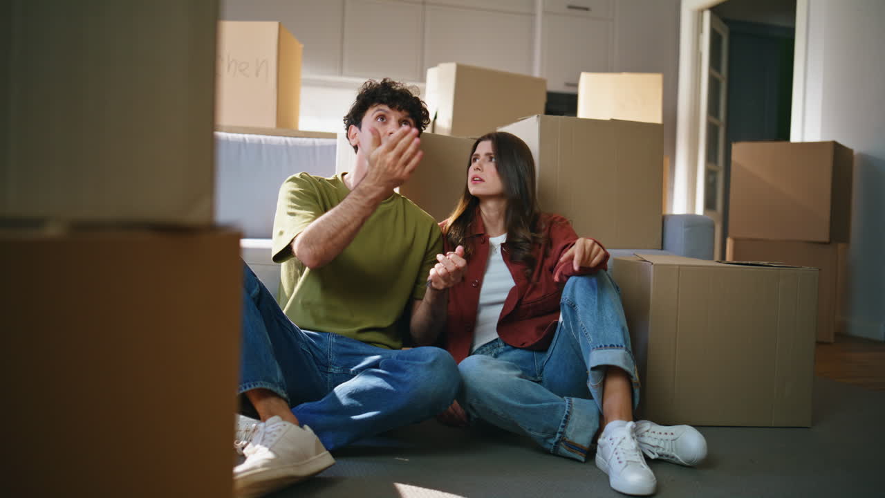 New homeowners discussing interior together around cardboard boxes. Couple rest