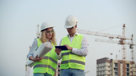 Zwei-Wirtschaftsingenieure-Tragen-Schutzhelme-Und-Halten-Ein-Tablet-In-Der-Hand.-Sie-Arbeiten-Als-Ingenieure-Und-Besprechen-Die-Inspektion-Von-Zeichnungen.-Draußen-An-Einem-Gebäude.-Technische-Werkzeuge.