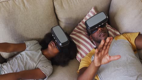 african american daughter and her father lying on couch wearing vr headsets