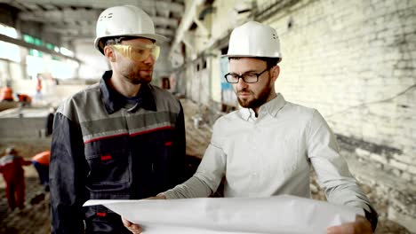 arquitecto y trabajador en el sitio de construcción de la planta. el arquitecto jefe examina el dibujo y decide sobre el trabajo adicional