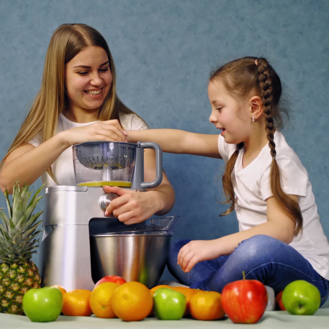 Bambina che prepara succo fresco. Madre allegra con figlia sedute al tavolo, mentre preparano succo fresco.