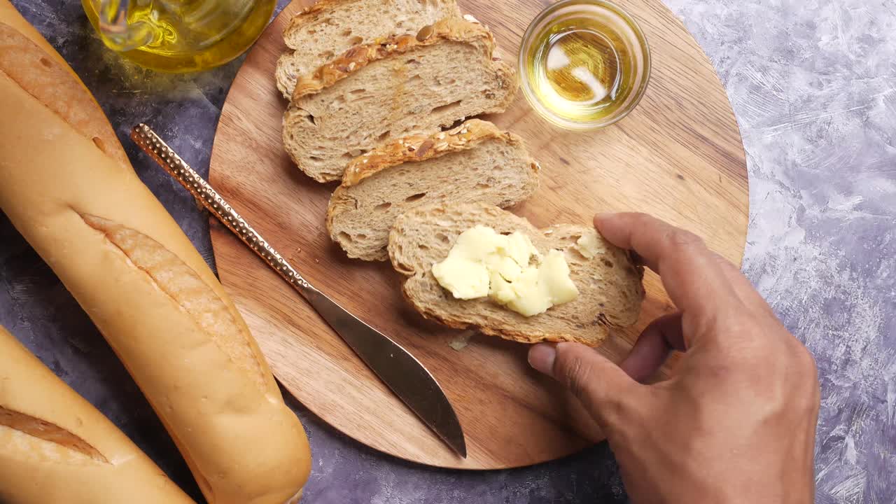 Hand reaching for a slice of buttered bread on a wooden board with olive oil