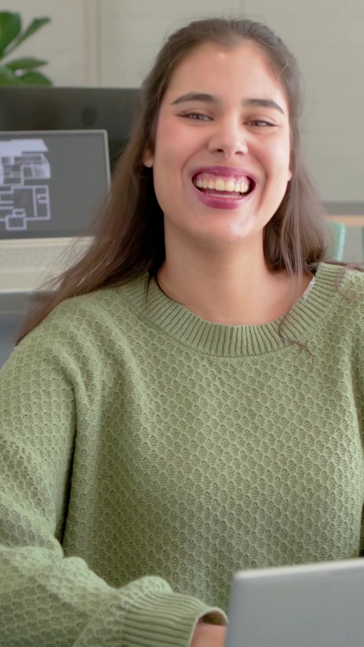 Impiegato che guarda il laptop e trasforma un sorriso in una risata aperta mentre reagisce a una chat divertente.