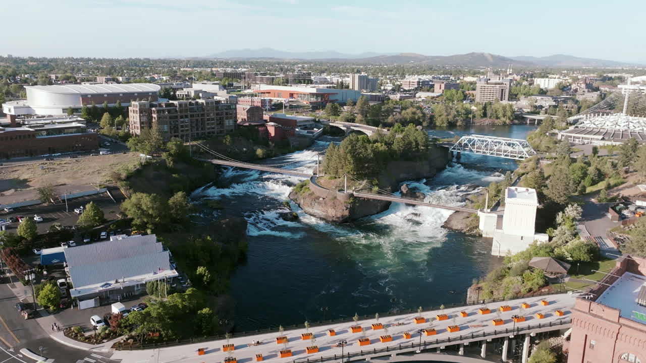Cars cross a bridge above the dam in downtown Spokane. The waterfall drops sharply below, surrounded by trees and buildings