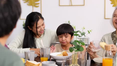 Four generations gather around a breakfast table in a bright, modern dining room. Natural lighting, warm atmosphere, and gentle camera movement highlight family connection