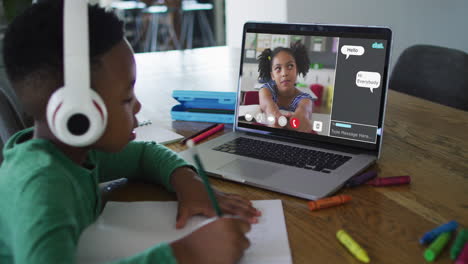 schoolboy using laptop for online lesson at home, with schoolgirl talking and web chat on screen