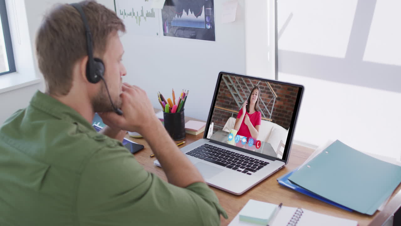 Kaukasisk mand bruger bærbar computer og telefonheadset på videoopkald med en kvindelig kollega.