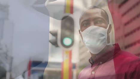 animation of flag of france waving over african american man wearing face mask in city street