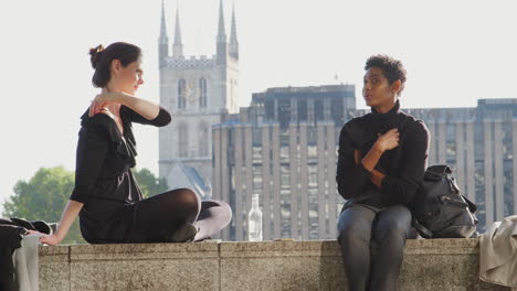 two young adult women sitting on the embankment at the thames riverside talking, backlit, close up