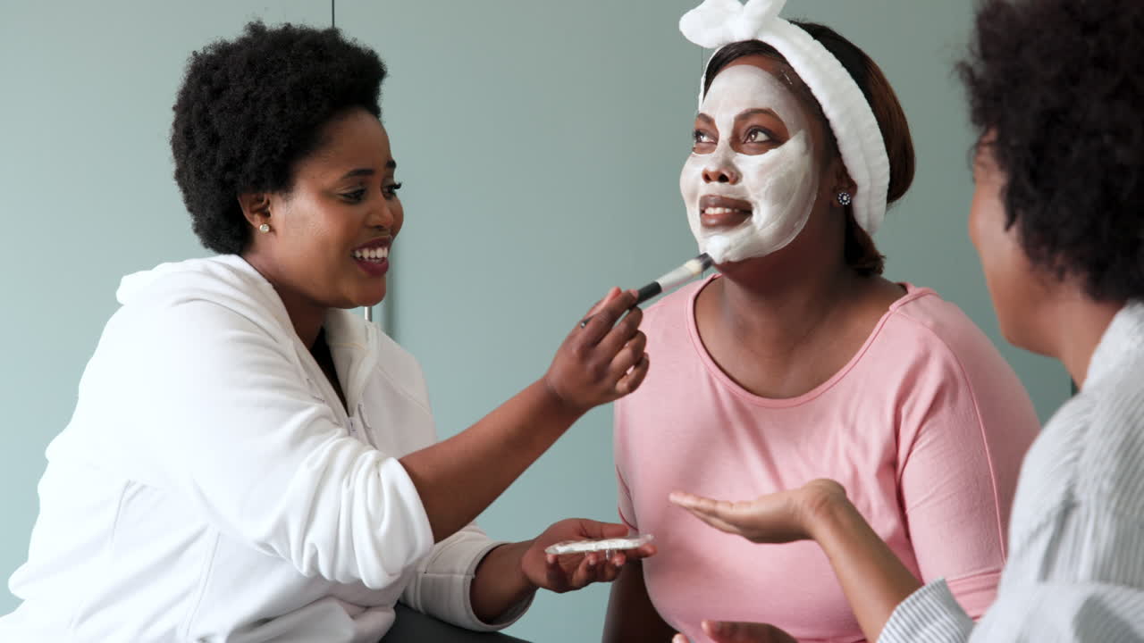 Laughing together, friends applying face masks during spa day at home