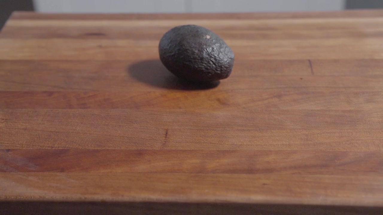 Un'inquadratura statica di un avocado che viene posizionato su un tagliere. Ideale per contenuti culinari, che evidenzia ingredienti freschi e l'inizio della preparazione del cibo