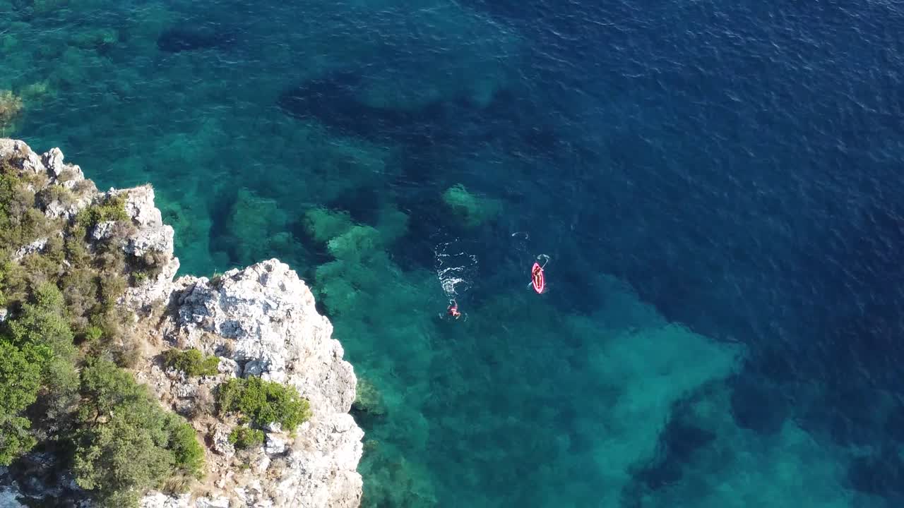 A man swimming and a man kayaking in the deep blue sea in Corfù island, Greece. Filmed by drone