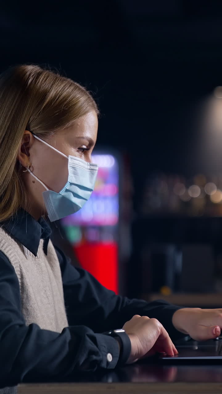 Portrait quarantine employee in mask. Pretty young lady in mask working with computer. Vertical video