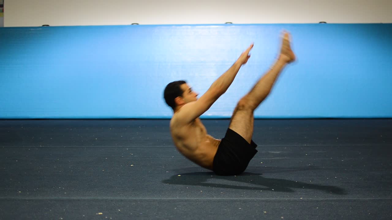 una toma estática de un tipo en un gimnasio de gimnasia haciendo ejercicios abdominales con levantamientos de piernas sin camisa desde una vista frontal lateral