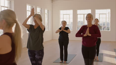 instructor de clase de yoga enseñando a mujeres maduras sanas practicando pose de oración disfrutando del ejercicio físico matutino en el estudio al amanecer.