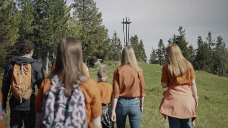 Young-scouts-walking-towards-the-statue-on-mountain-Črni-vrh,-wearing-orange-shirts-and-backpacks,-leisurely-talking