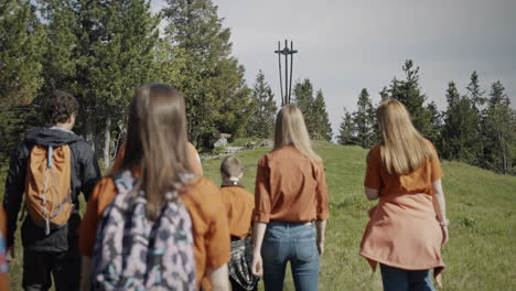 young scouts walking towards the statue on mountain črni vrh, wearing orange shirts and backpacks, leisurely talking