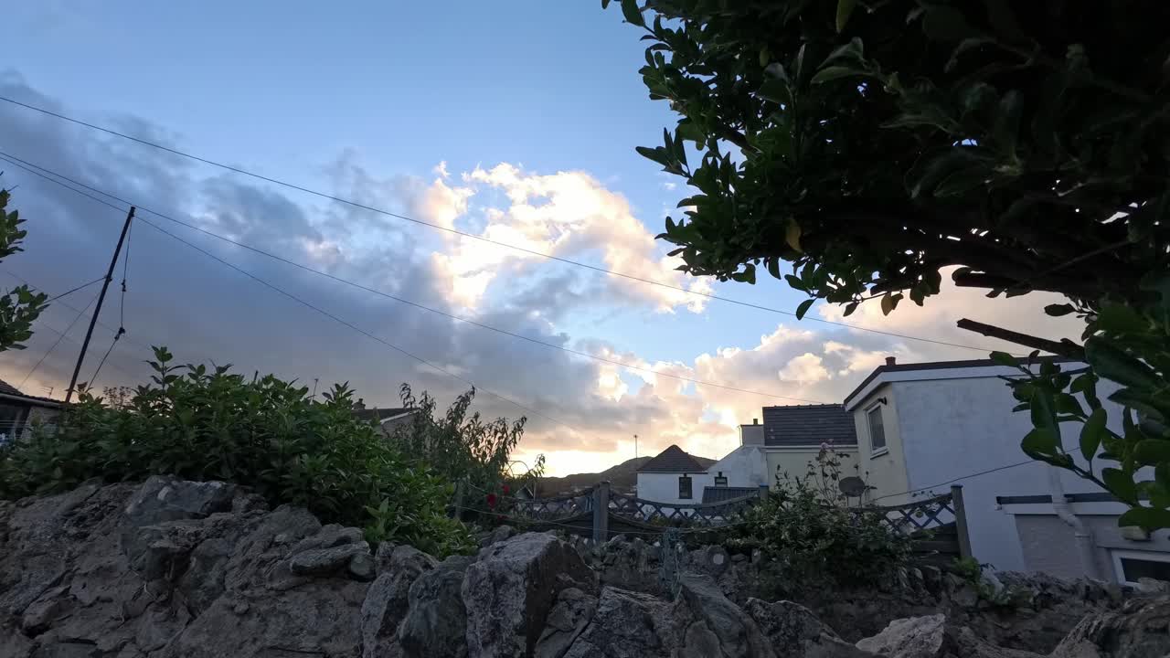 Time lapse sunset clouds passing over rural Welsh cottage stone garden wall with windy trees