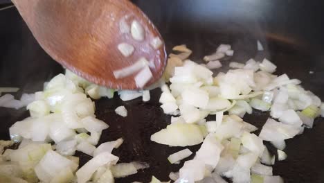 General cooking footage, slow zoom in of onions and garlic frying in a pan.