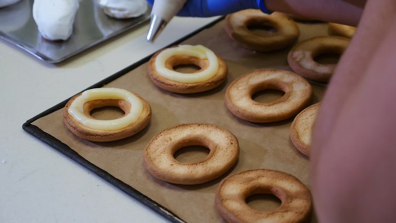 Pastry chef filling baked doughnuts with pastry cream using a piping bag. Handmade preparation of traditional desserts