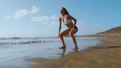 beautiful girl athlete with beautiful breasts in black shorts and a white top crouches and makes a jump up. circular training for the heart. slow motion steadicam