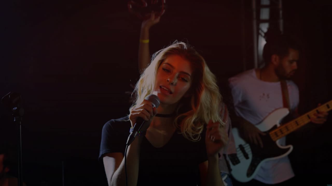 Lead singer holding wired mic and lifting hand, causing sparks while delivering intense music set