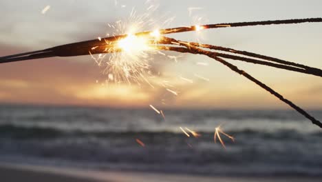 lit sparklers glowing, with sea and sunset in background