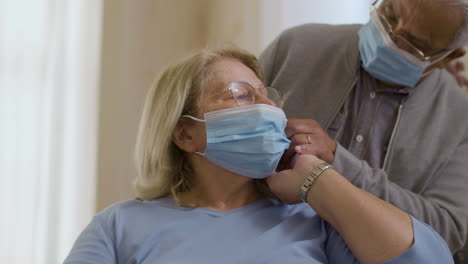 medium shot of man helping wife putting on protective mask