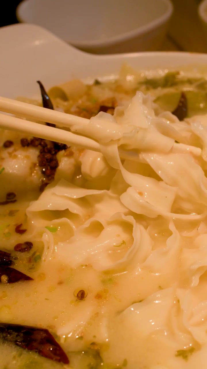 Primo piano di bacchette che sollevano noodles larghi da una ciotola di zuppa di pesce piccante.