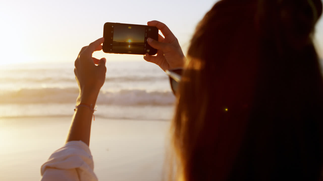 mujer tomando una foto con un teléfono móvil en la playa 4k