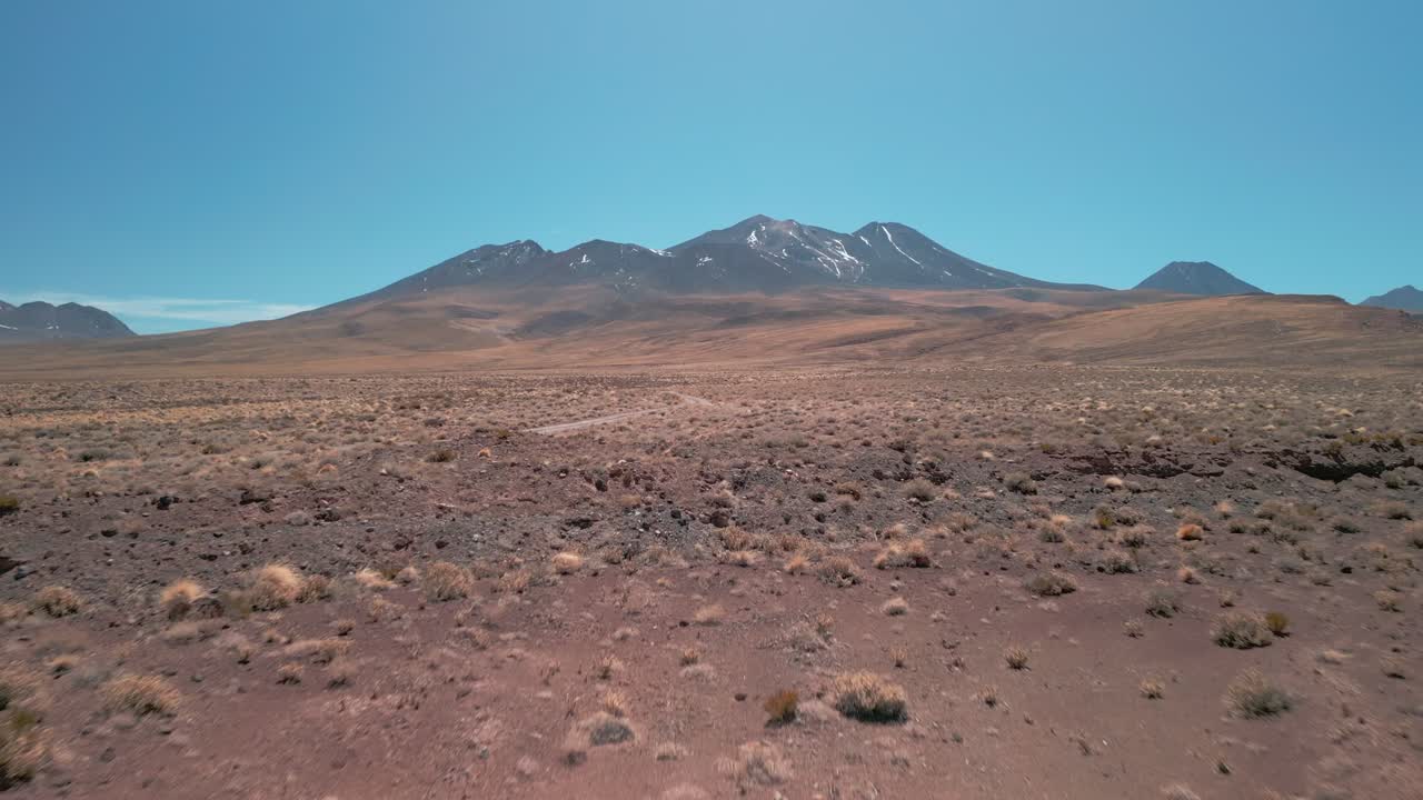 disparo de drones yendo a un volcán en el desierto chileno pasando cerca de la vegetación seca que está en el suelo y luego sobre una carretera