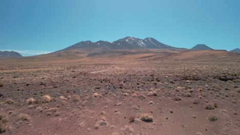 Drone-shoot-going-to-a-volcano-in-the-Chilean-desert-passing-near-the-dry-vegetation-that's-on-ground-and-then-over-a-highway