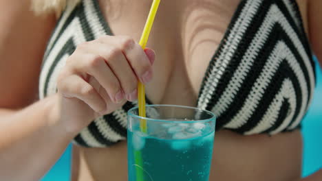 woman in bikini shatters ice in a cocktail, close-up